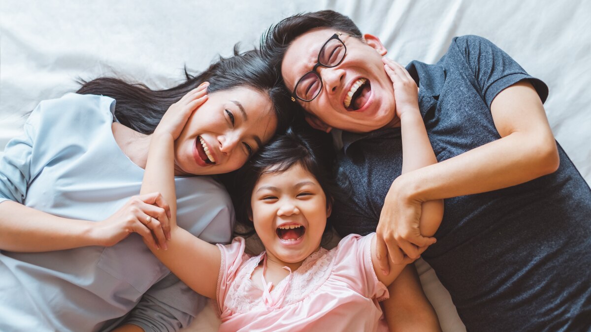 Smiling parents and child lying on bed, laughing and hugging closely in a joyful family moment.
