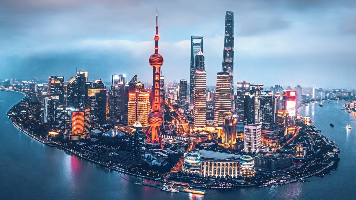 Aerial view of Shanghai skyline at dusk featuring the Oriental Pearl Tower, modern skyscrapers, and the Huangpu River illuminated by city lights.