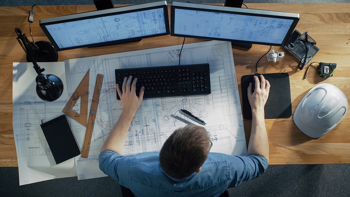 Engineer drafting workspace with blueprints and dual monitors