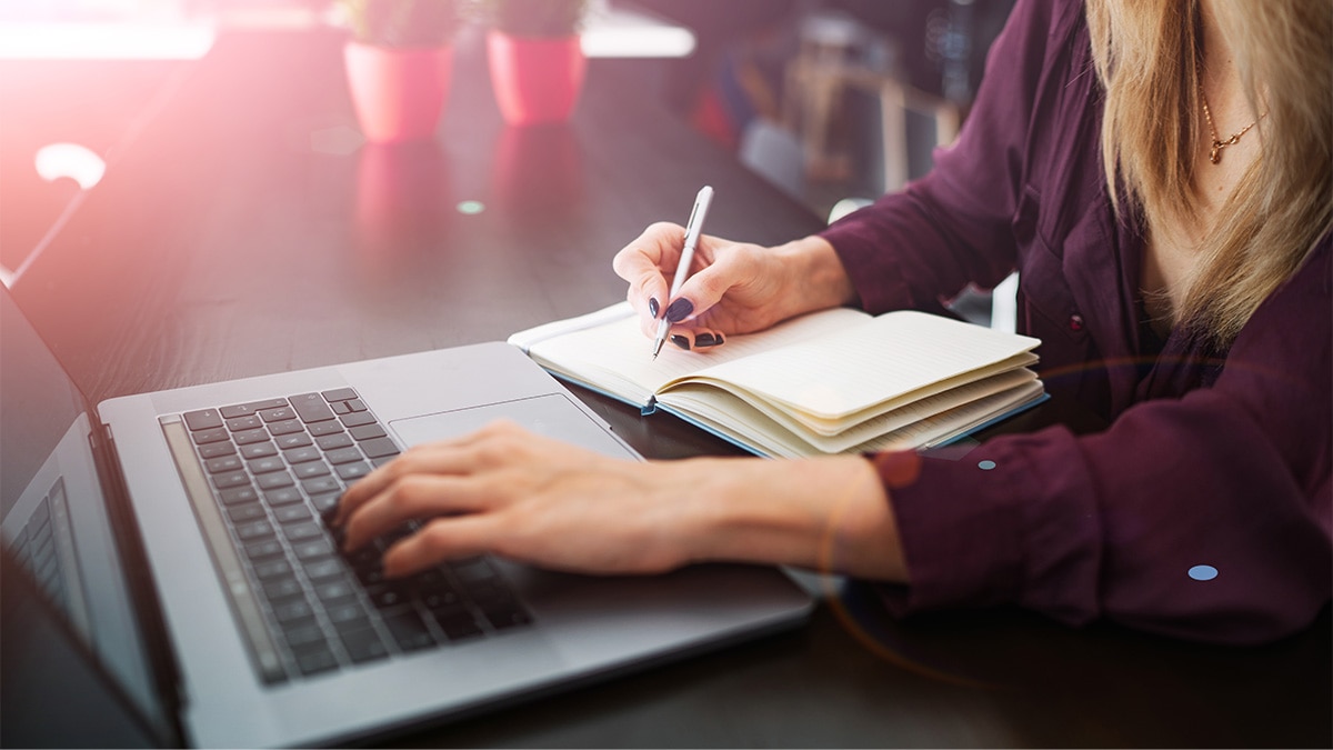 woman using laptop writing in a book