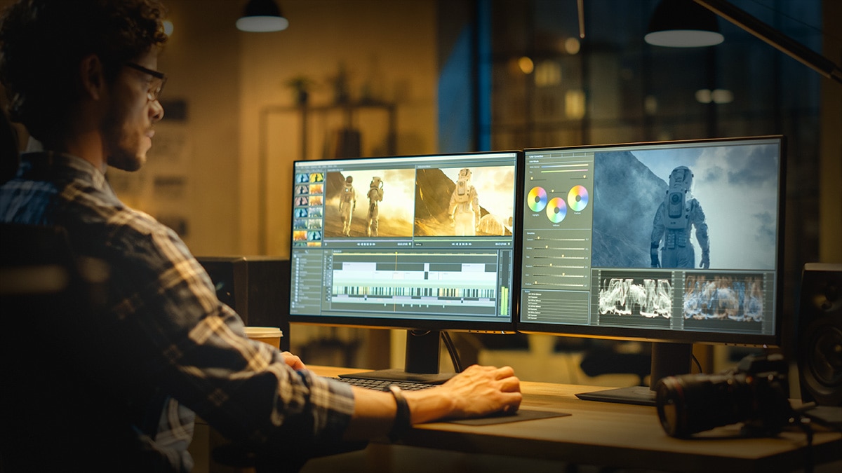 man looking at computer monitors editing videos