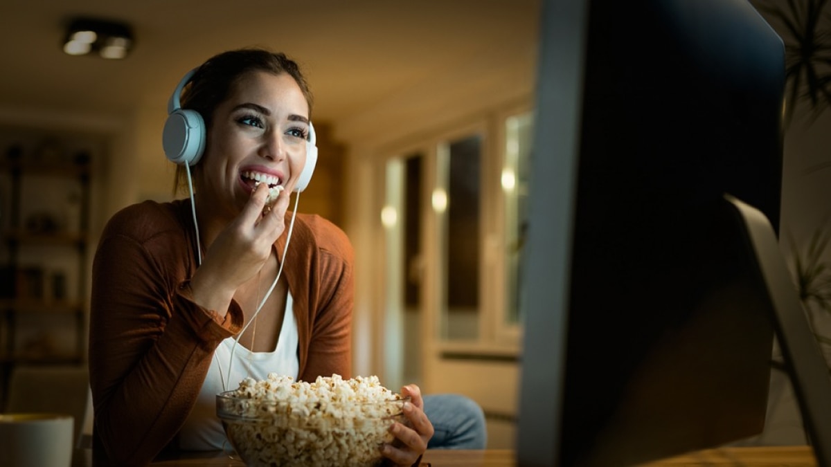 woman eating popcorn looking at computer screen woman eating popcorn looking at computer screen
