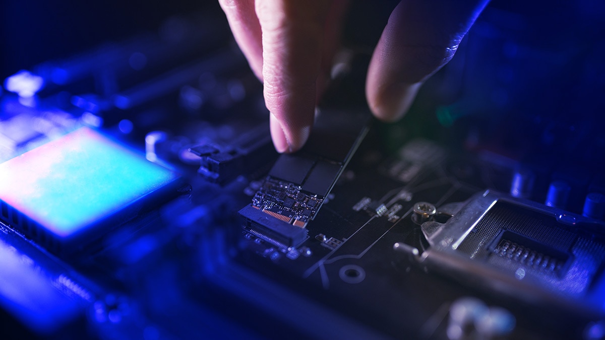 Focus at SSD slot, type M.2 with support for NVMe, on computer motherboard. Technician is installing new fast high capacity drive with flash chips, known as SSD.