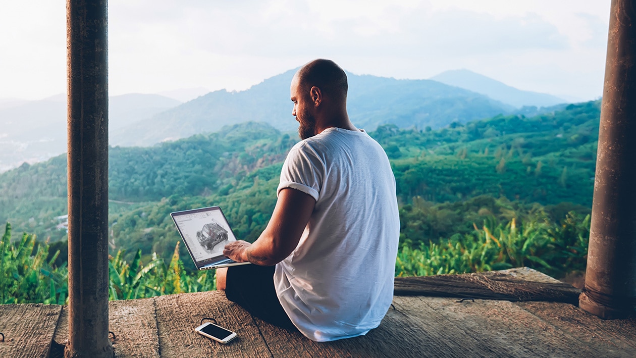 Man working remotely on a laptop with mountains in the background Man working remotely on a laptop with mountains in the background
