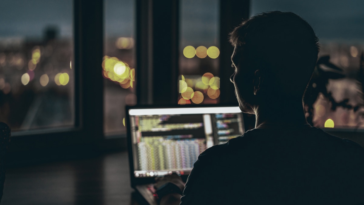 Man on computer in a dim room with a city view.