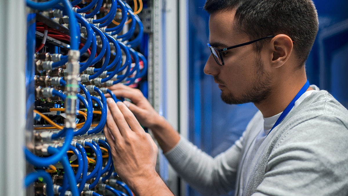 Side view portrait of young man connecting wires in server cabinet while working with supercomputer in data center