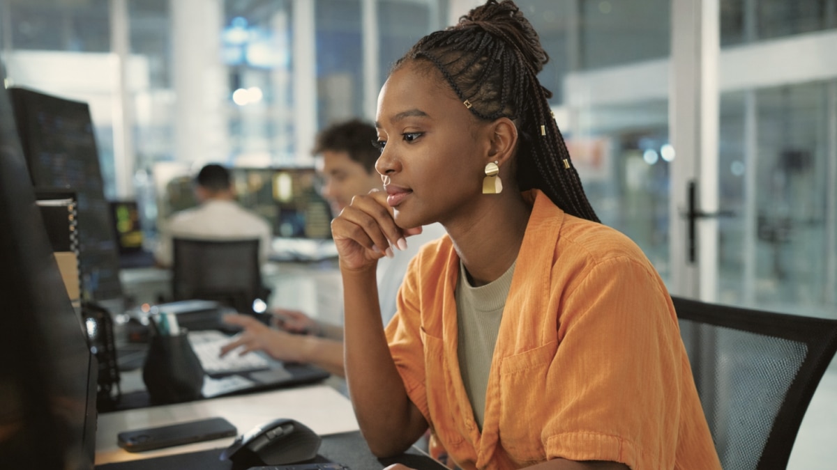 Professional woman in orange shirt works at desktop computer in contemporary office setting