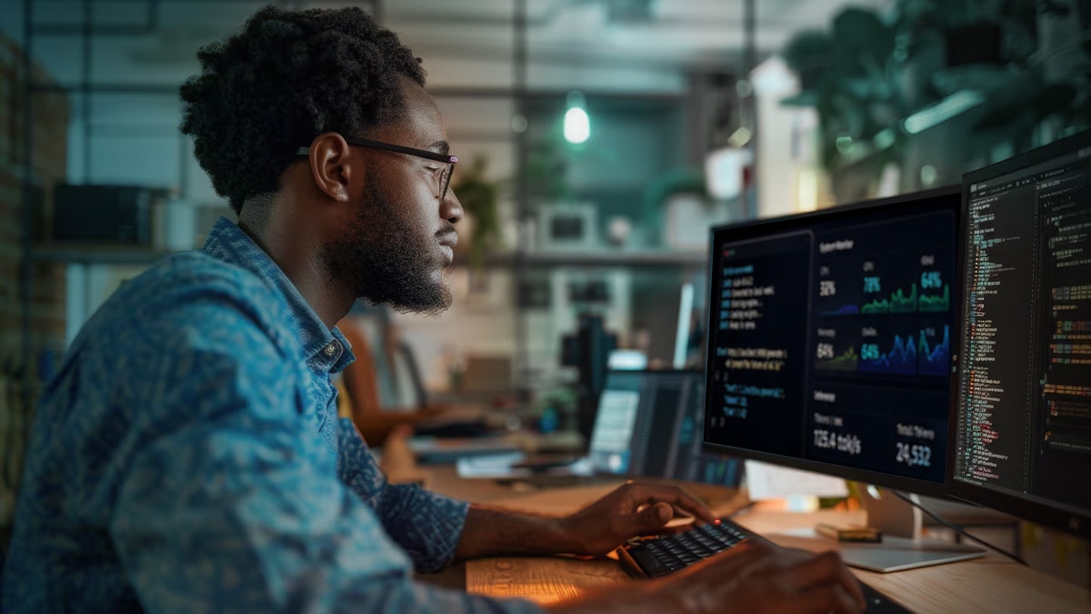 Man in blue shirt and glasses coding and monitoring data on two screens