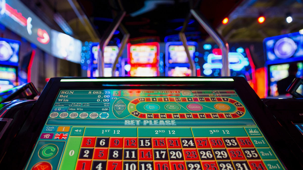 Blurred gaming machines with bright blue, red, and green screens in a dark casino-like setting, a person visible.