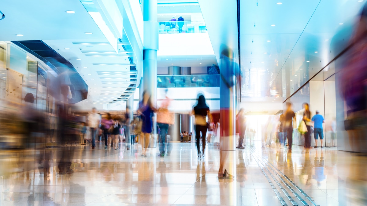 Blurred people walk through a bright, modern interior with blue and white lighting, polished floors, and multiple levels.