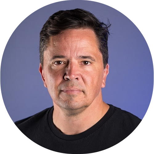 Man with short dark hair wearing a black shirt against a blue background.