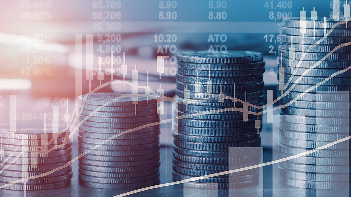 Stacks of coins overlaid with rising financial charts and stock market data in blue tones.